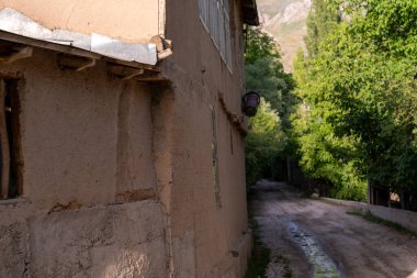 Yan tarafında bir ev olan toprak bir yol. Ev taştan yapılmış ve penceresi var.