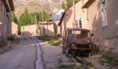 Paslı eski bir araba bir sıra evin önündeki toprak bir yolda park edilmiş. Sahne sessiz ve huzurlu, görünen tek nesne araba.