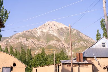 Bir köyün arkasında bir dağ sırası görülebilir. Gökyüzü açık ve mavidir, ve güneş parlıyor. Köy çatısı ve bacası olan küçük evlerden oluşuyor.