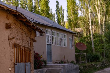 Çatıda kırmızı uydu anteni olan küçük bir ev. Ev ağaçlarla çevrili ve önünde bir bahçe var.