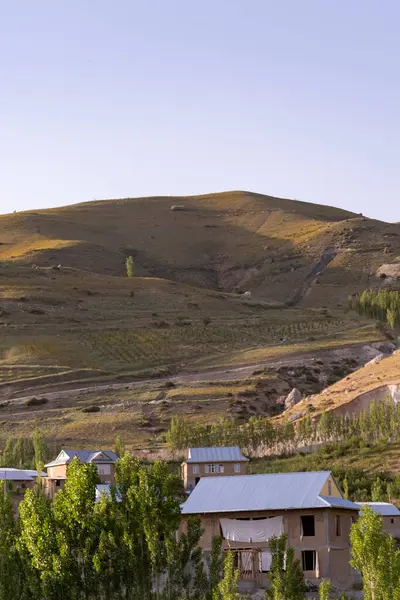 Üzerinde evler olan bir dağ silsilesi. Evler küçük ve çatıları var. Gökyüzü mavi ve güneş parlıyor.