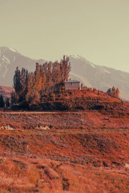 Tepesinde bir ev olan bir dağ sırası. Ev ağaçlarla çevrili ve dağlar karla kaplı. Huzurlu ve huzurlu bir sahne.