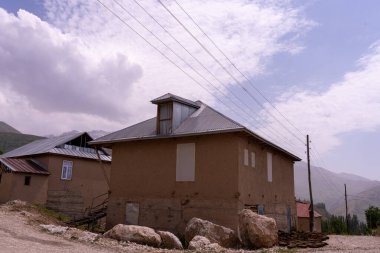 Eğimli çatılı küçük bir ev kayalık bir yamaçta duruyor. Ev kayalar ve tellerle çevrili. Gökyüzü bulutlu ve ev izole edilmiş gibi görünüyor.