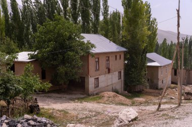 Önünde ağaç olan küçük bir ev. Ev ağaçlarla çevrili ve çatısı var.