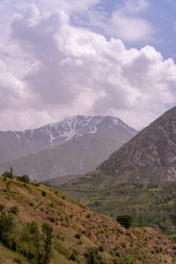 Gökyüzü bulutlu ve dağlar karla kaplı. Dağlar çok yüksek ve onları kar kaplıyor.