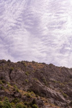 Arkasında bulutlu bir gökyüzü olan bir dağ. Gökyüzü çoğunlukla beyaz bulutlarla mavidir.