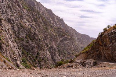 İkisinin arasında kayalık, çorak bir vadi olan bir dağ sırası. Gökyüzü bulutlu ve dağlar ağaçlarla kaplı.