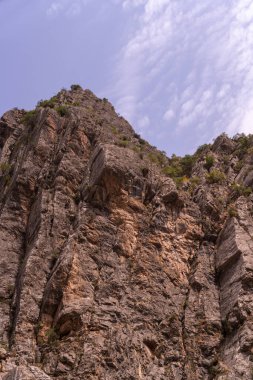 Arka planda mavi gökyüzü olan kayalık bir dağ. Gökyüzü açık ve güneş parlıyor.