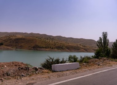 Beyaz taştan bir bariyer ve arka planda su kütlesi olan bir yol. Su sakin ve berrak.