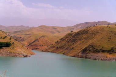 İçinden bir nehir akan güzel bir dağ sırası. Su koyu mavi bir renktir. Dağlar çimlerle ve ağaçlarla kaplı.