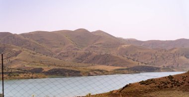 Önünde bir su kütlesi olan güzel bir dağ sırası. Gökyüzü açık, dağlar ise ağaçlarla çevrili.