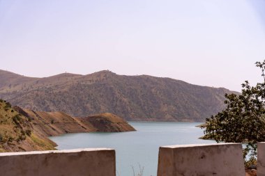 Arka planda dağlar olan güzel bir göl manzarası. Su durgun ve berrak, dağlar ise ağaçlarla kaplı. Sahne huzurlu ve huzurlu, ve bir huzur hissi uyandırıyor.