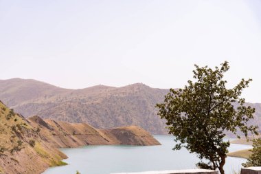 Önünde göl olan bir dağ sırası. Göl mavi ve dağlar kahverengi.