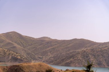 Önünde göl olan bir dağ sırası. Gökyüzü açık ve güneş parlıyor.