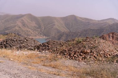 Önünde bir su kütlesi olan bir dağ sırası. Dağlar kayalarla kaplı ve su sakin.