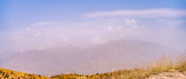 Uzakta açık mavi gökyüzü ile bir dağ sırası görülebilir. Dağlar karla kaplı ve gökyüzü berrak.