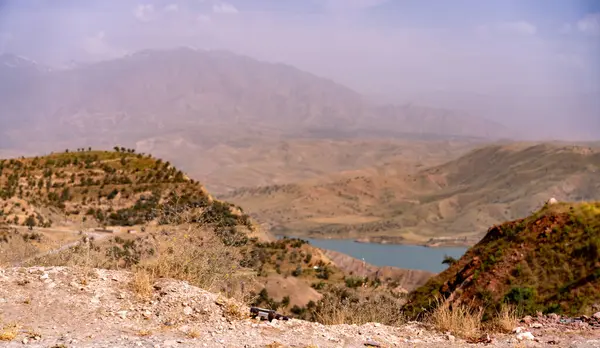 Uzakta gölü olan bir dağ sırası. Gökyüzü bulutlu ve dağlar ağaçlarla kaplı.