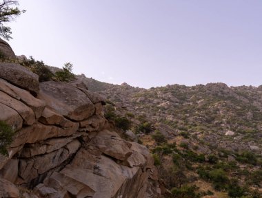 Arka planda açık mavi gökyüzü olan kayalık bir yamaç. Gökyüzü bulutlarla dolu, ortama huzurlu ve huzurlu bir atmosfer veriyor.