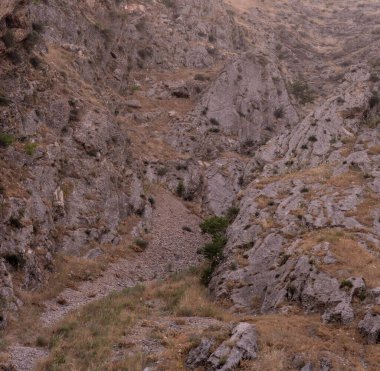 İçinden akan küçük bir deresi olan kayalık bir yamaç. Kayalar büyük ve pürüzlü ve çimenler seyrek. Sahne, kabalık ve izolasyondur.