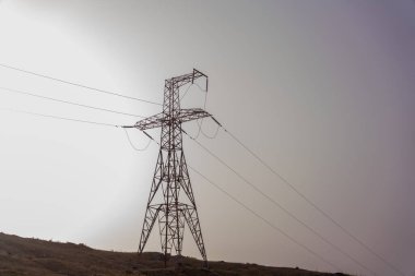 Bulutlu gökyüzüne karşı uzun bir güç hattı kulesi silueti var.