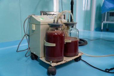 Üzerine iki tüp bağlanmış tıbbi bir cihaz. Tüpler kırmızı sıvıyla dolu. Cihaz mavi bir yüzeyde.