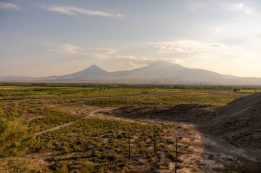 Arkasında dağ sırası olan uçsuz bucaksız, boş bir çöl. Gökyüzü açık ve güneş parlıyor.