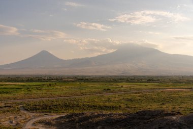 Ortasında yol olan bir dağ sırası. Gökyüzü bulutlu ve güneş batıyor.