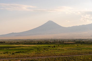 Arkasında büyük bir dağ olan bir dağ sırası. Gökyüzü bulutlu ve güneş parlıyor