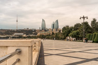 Arkasında büyük bir bina olan bir şehir parkı. Park boş, etrafta dolaşan birkaç kişi dışında.