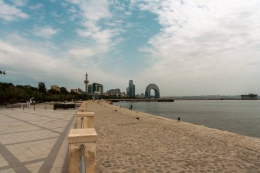 Arkasında şehir olan bir sahil. Kumsal boş ve gökyüzü bulutlu. Şehir uzakta ve su sakin.