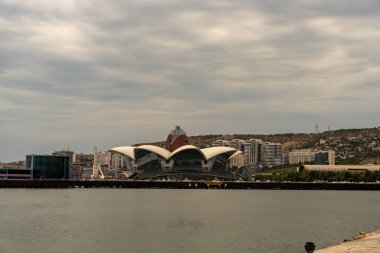 Uzakta tepesinde kubbe olan büyük bir bina görülüyor. Gökyüzü bulutlu ve su sakin.
