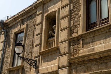 Yanında lamba direği ve heykeli olan bir bina. Bina eski ve çok detay içeriyor.