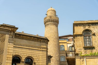 Üzerinde kule ve saat olan yüksek bir bina. Binanın etrafı başka binalarla çevrili ve bir sürü penceresi var.