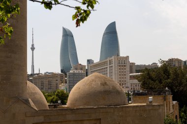 İki yüksek binası ve arka planında büyük bir kulesi olan bir şehir. Binalar taştan yapılmış ve tepesinde kubbeler var. Şehir eski ve yeni mimarinin bir karışımı gibi görünüyor.