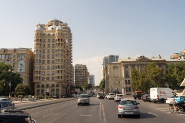 Arabaları ve bisikleti olan kalabalık bir cadde. Sahne hareketli ve canlı.