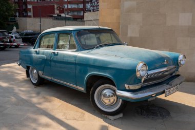 Bir binanın önünde mavi bir vintage araba park edilmiştir. Araba eski ve klasik bir tasarımı var.