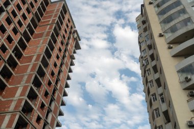 Bir tanesi yapım aşamasında olan iki bina gökyüzünde gösteriliyor. Bulutlar beyaz ve kabarık, barışçıl bir atmosfer yaratıyorlar.