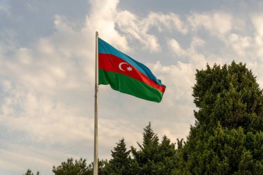 Üzerinde Azerbaycan yazan bir bayrak havada dalgalanıyor. Gökyüzü bulutlu ve bayrak yeşil, mavi ve kırmızı