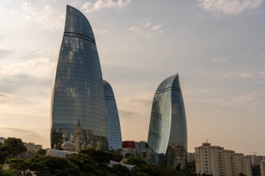 İki uzun bina, bir sürü cam pencere ve arka planda bulutlu bir gökyüzü. Binalar çok yüksek ve eşsiz bir şekli var.