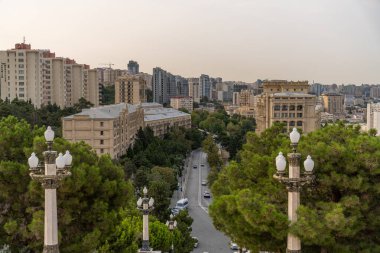 Uzun binaları ve ağaçlarla kaplı kaldırımları olan bir şehir caddesi. Sokaklar arabalar ve yayalarla dolu.