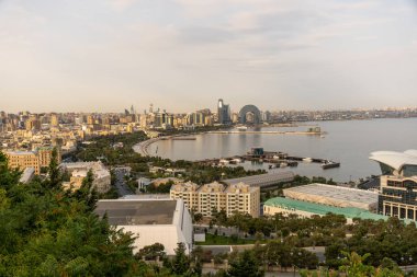 Arka planda büyük bir su kütlesi olan bir şehir manzarası. Şehir yüksek binalarla dolu ve su sakin.