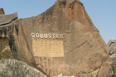 Üzerinde Qobustan yazan büyük bir kaya. Kaya yeşil bir alanla çevrili.