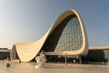 Önünde beyaz bir heykel ve kıvrımlı bir çatısı olan büyük bir bina. Bina çok yüksek ve bir sürü penceresi var.