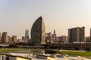 Ortasında yüksek bir bina olan bir şehir silueti. Gökyüzü açık ve güneş parlıyor.