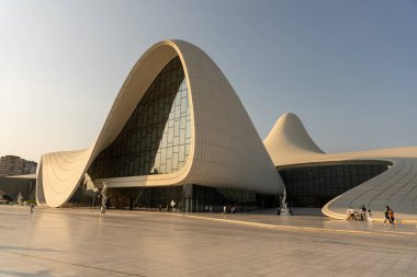 Kavisli çatısı ve bir sürü penceresi olan büyük bir bina. İnsanlar binanın etrafında dolanıyor.