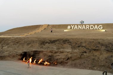 Üzerinde YANARDAG yazan büyük bir tabela. İşaret ateşle yanıyor, dramatik ve dikkat çekici bir sahne yaratıyor.