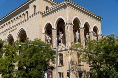 Önünde kavisli pencereler ve heykeller olan büyük bir bina. Bina kahverengi ve çok detay içeriyor.