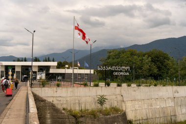 Üzerinde Georgia yazan bir binanın üstünde bir bayrak dalgalanıyor. Gökyüzü bulutlu ve arkadaki dağlar görülebilir.