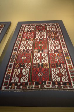 Kare ve üçgen desenli bir halı bir müzede sergilenir. Halı kırmızı ve beyaz ve çok detay içeriyor.