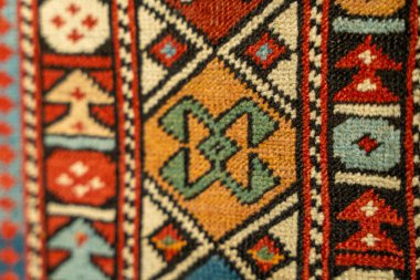 Kare ve üçgen desenli renkli bir halı. Halı yünden yapılmıştır ve mavi ve kırmızı şeritlidir.